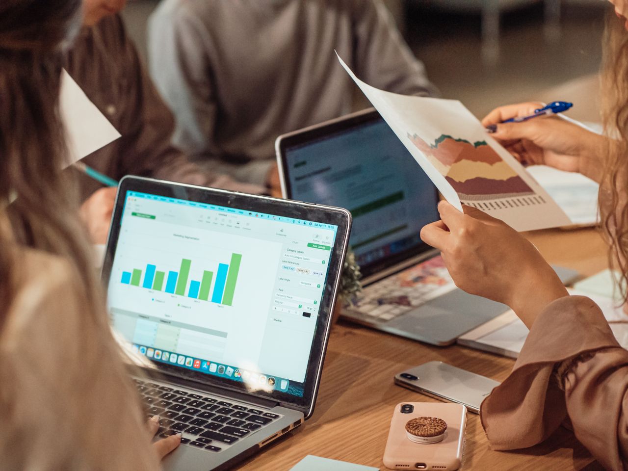Un groupe réuni en réunion professionnelle, analysant des graphiques sur des ordinateurs portables et des documents papier.
